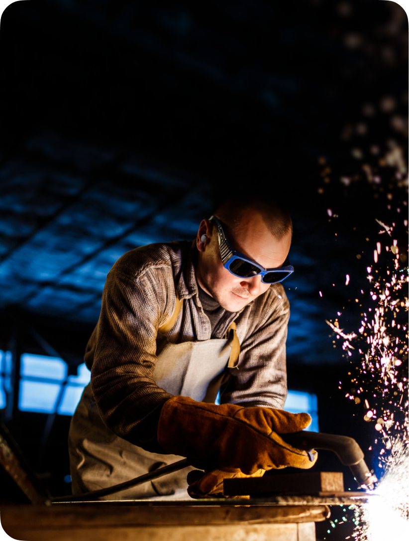 Person welding with sparks flying in a dark workshop setting