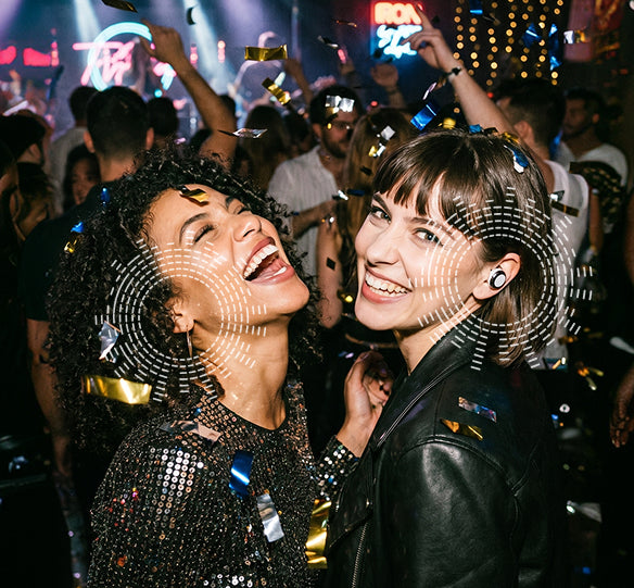 Two women laughing together at a party with confetti and lights in the background